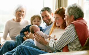 Multi Generation Family Sitting On Sofa With Newborn Baby Smiling